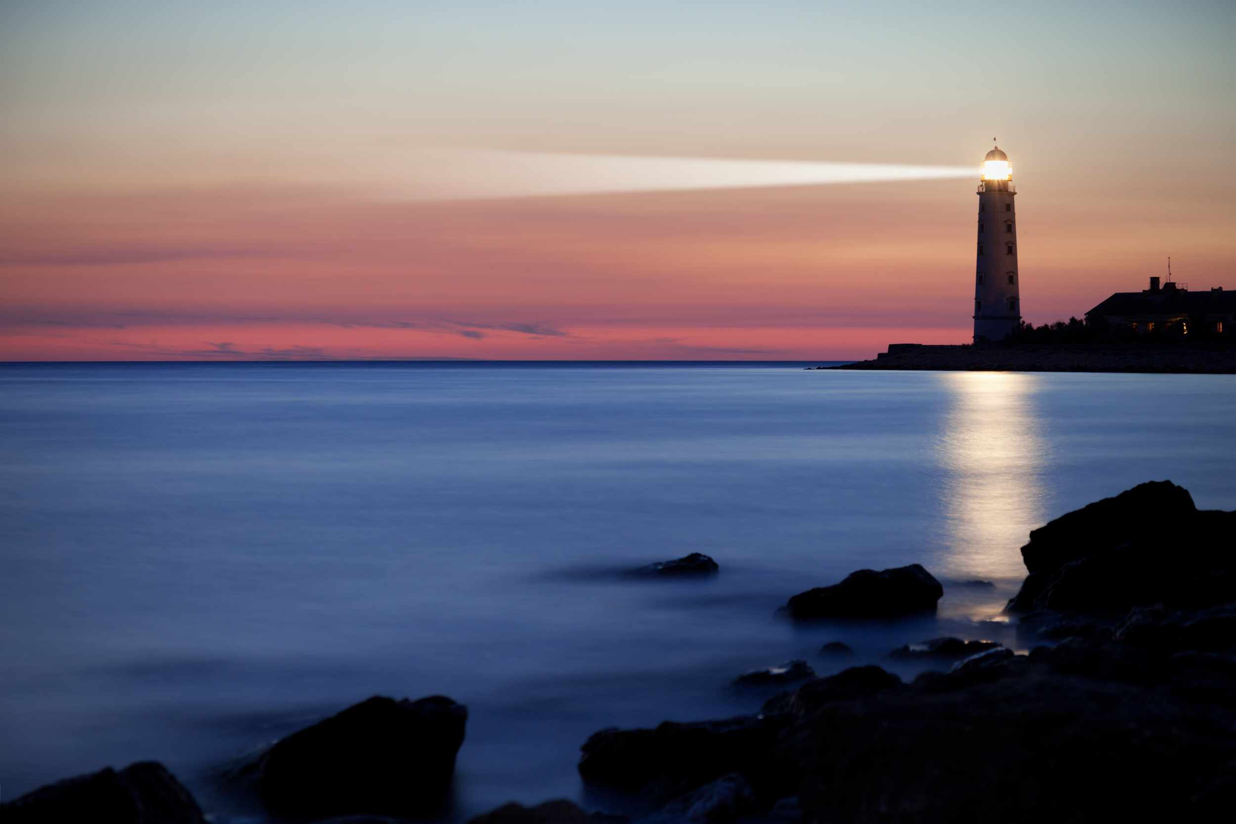 A lighthouse emitting a beam of light over water at dusk