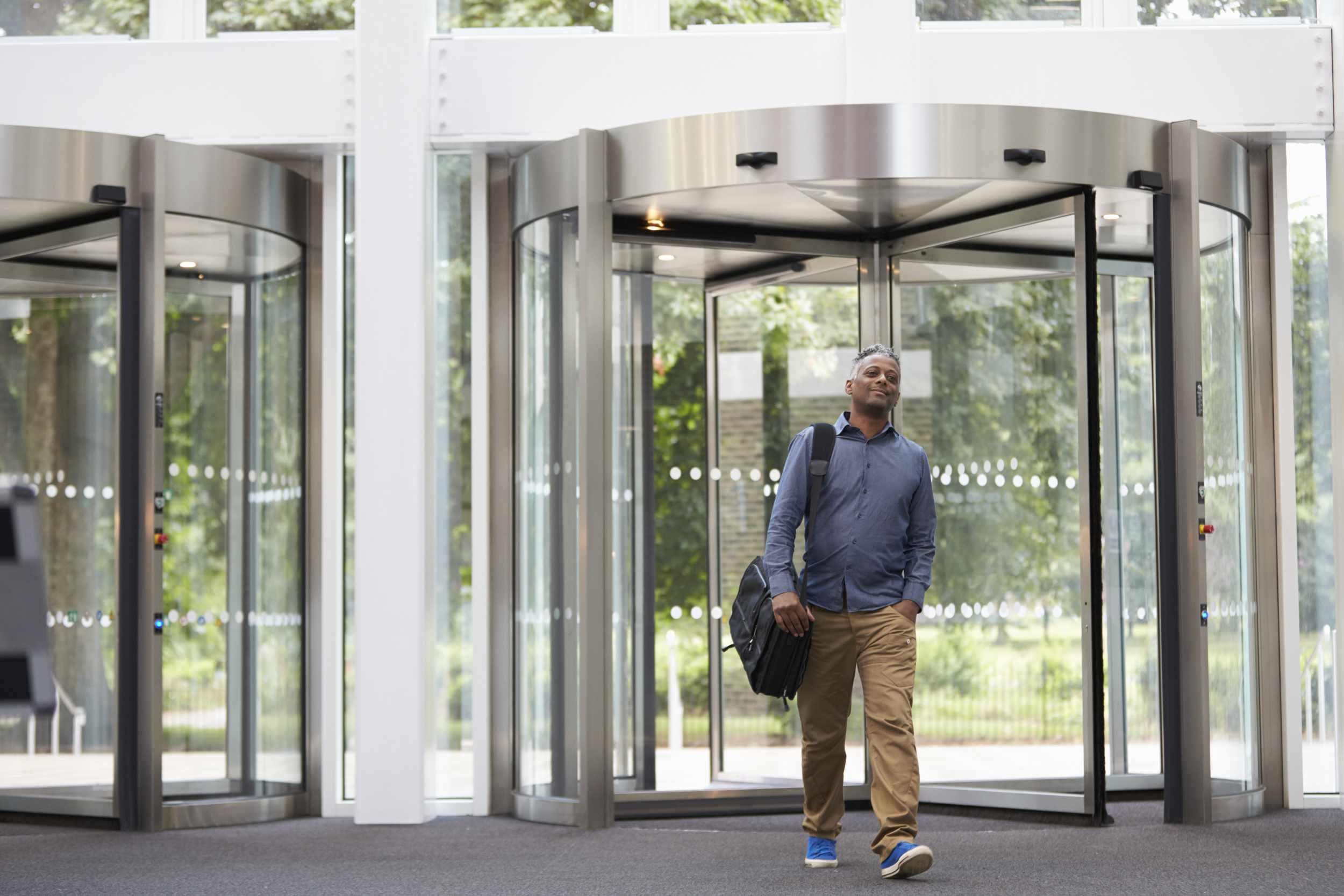 A man with a bag over his shoulder walking out of a revolving door