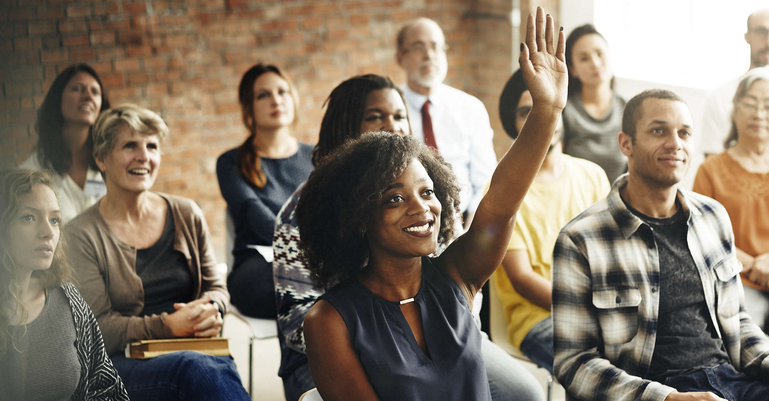 People seated in a classroom with one woman raising a hand